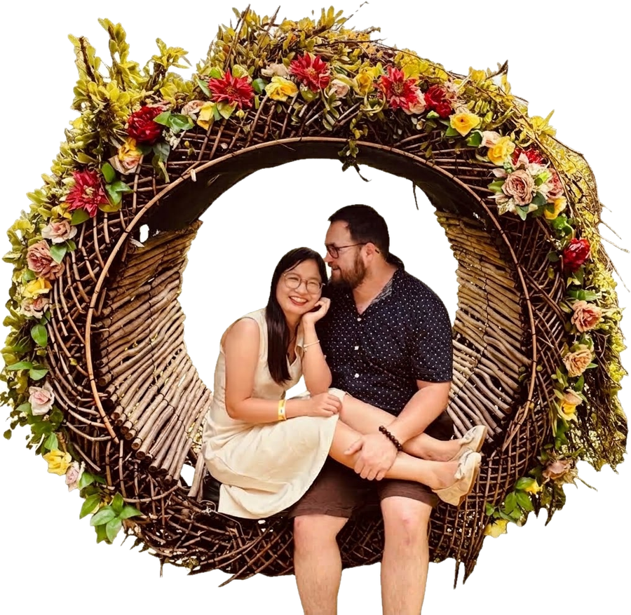 Trang and Robert sitting together inside a large round wreath of woven twigs decorated with flowers