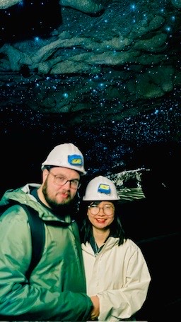 Trang and Robert in hard hats under the blue glow-worms of the Waitomo caves