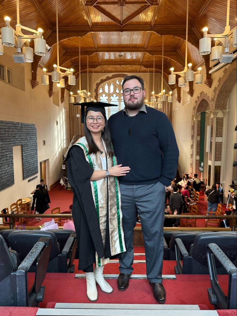 Trang in cap and gown with Robert at her graduation in the university hall